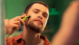 Taghareed Philips OneBlade QP2824/10 electric trimmer with green accents, used by a man to trim his beard.