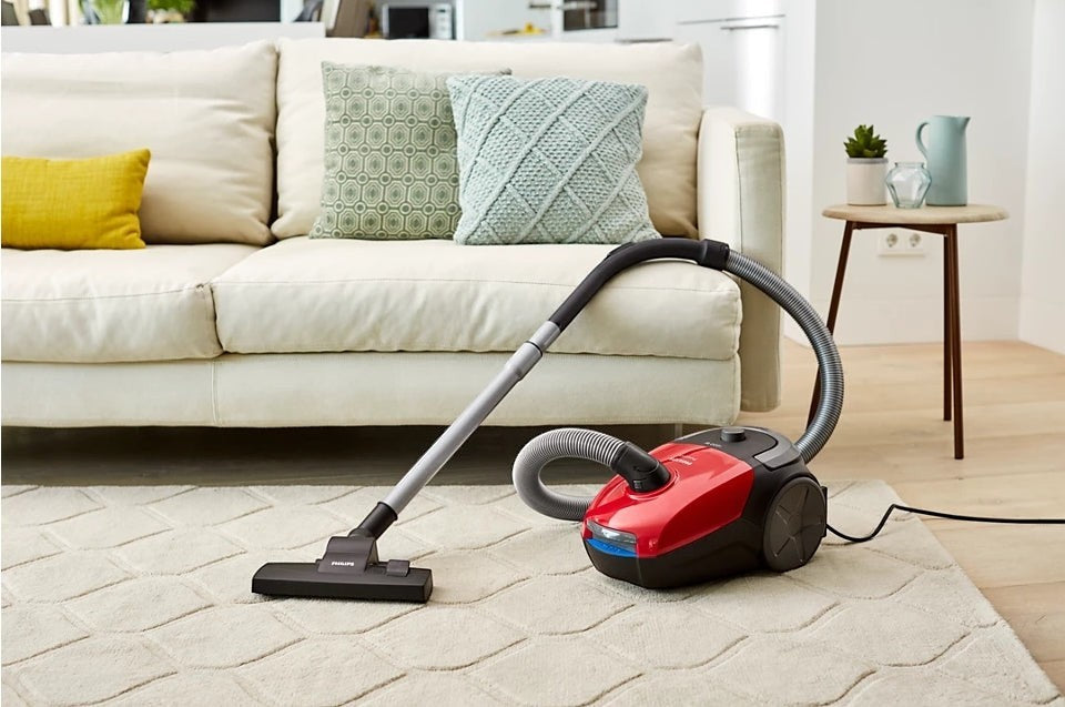 Taghareed Philips 2000 Series bagged vacuum cleaner in red and black, with multi-purpose nozzle on a cream rug.