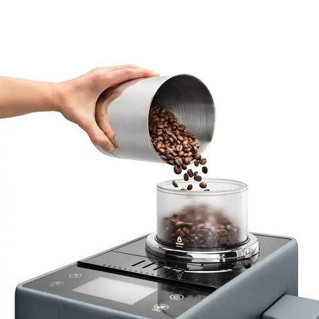 Taghareed Rivelia automatic coffee machine with dual bean hoppers, pouring coffee beans into the grinder.